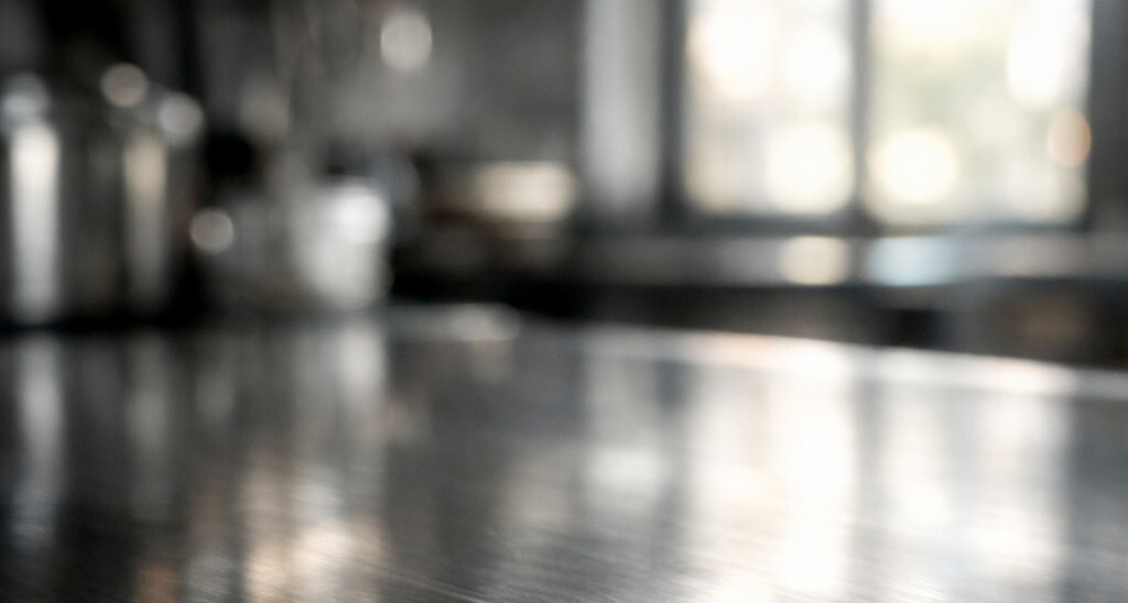 Capture a highcontrast macro shot of a polished stainless steel kitchen surface reflecting the soft glow of natural light filtering through a nearby w-1